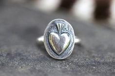 This listing is for one beautifully unique sterling silver sacred heart ring. The sacred heart features a simple heart with radiant lines faintly on the center and a triple flame on top. It is fired onto sturdy 9 gauge sterling silver half round wire. This ring is made using a steel die replica of a vintage Catholic medal, forging molten sterling silver into the shape using my hydraulic press. Wear this ring solo for simple elegance of wear it stacked with several hammered bands for an edgier, bohemian style! - Choose your ring size and stacking options at checkout!  - Sacred Heart measures 19mm by 14mm. - Made to Order: please see current processing times in Shipping Info and Shop Announcement. See more sacred hearts here:  https://www.etsy.com/shop/DeerGirlDesigns?ref=profile_header&sect Burning Heart, Flaming Heart, Hydraulic Press, Fire Ring, Sweet Ring, The Sacred Heart, Jewelry Heart, Catholic Medals, Hammered Band