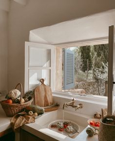 a kitchen sink sitting under a window next to a counter top with fruit and vegetables on it