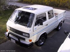 a small white truck parked in a parking lot next to a car and another vehicle