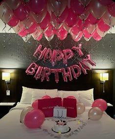 a bed with pink and red balloons on top of it next to a birthday cake