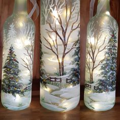 three glass bottles decorated with christmas trees and lights