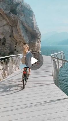 a woman riding a bike down a wooden walkway next to the ocean on a sunny day