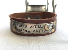 *This listing is for one hand made leather cuff measuring 3/4" wide with a metal piece which is soldered and then hand stamped with   stay WILD moon child    with a moon off to the side.*Sizing options:  The Regular size option is a cuff that will fit a wrist which is 6 1/2" up to 7".   The Large size option is a cuff that will fit a wrist which is 7 1/4" up to 8".  The XLarge size option is a cuff that will fit a wrist 8 1/4" up to 9".  If you are unsure of which size is right for you, please c Adjustable Engraved Cuff Bracelet With Meaningful Style, Adjustable Engraved Cuff Bracelet Meaningful Style, Adjustable Engraved Cuff Bracelet, Adjustable Stamped Leather Bohemian Bracelet, Spiritual Adjustable Hand Stamped Bracelets, Adjustable Spiritual Hand Stamped Bracelets, Adjustable Hand Stamped Leather Bracelet As Gift, Adjustable Leather Cuff Bracelet With Stamped Details, Rustic Stamped Leather Bracelet Gift