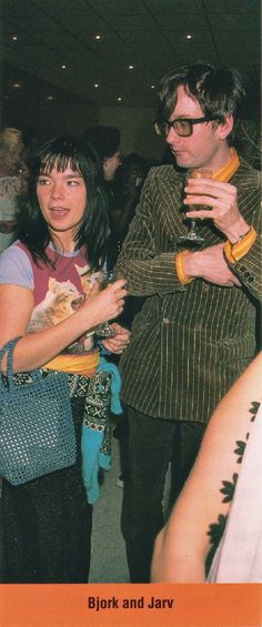 a man and woman standing next to each other at a party with drinks in their hands