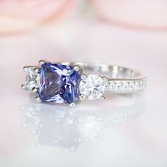 Gorgeous Princess Tanzanite Ring ►Made of sterling silver, rhodium plated (S925) ►Center stone: Tanzanite Color: Purple Gemstone Creation: Simulated Cut: Princess Gem size: 6.0 mm Carat Weight: 1.2 ct. (approx.) ►Accented with simulated diamonds (CZ) Cut: Round Gem size: 1.0 mm- 4.0 mm Color: Colorless ►Bands width: 2.4 mm ✓ 100% Nickel-Free ✓ Hypoallergenic ✓ Comfort Fit ✓ Free Ring Box ✓ Free USA Shipping ✓ Ready to ship next business day Classic Birthstone Ring With Accent Stones For Promise, Classic Promise Ring With Birthstone And Accent Stones, Classic Promise Birthstone Ring With Accent Stones, Classic Sapphire Ring With Accent Stones For Promise, Classic Promise Jewelry With Accent Stones, Classic Princess Cut Jewelry With Accent Stones, Classic Crystal Ring With Accent Stones For Promise, Classic Three Stone Crystal Promise Ring, Classic Birthstone Ring With Accent Stones For Anniversary