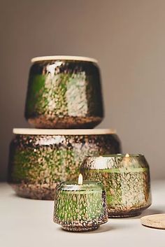 three green vases sitting next to each other on a white counter top with one candle in the middle