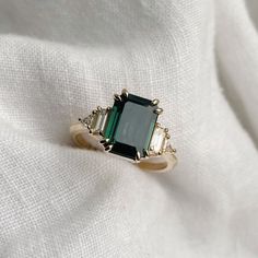 an emerald and diamond ring sitting on top of a white cloth