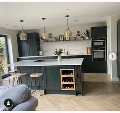 a kitchen with green cabinets and an island in the middle is filled with wine bottles