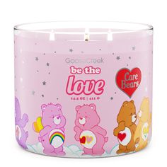 a pink candle that says be the love with bears and rainbows on it, in front of a white background