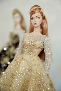 two barbie dolls are dressed in gold and silver dresses, one is wearing a dress with sequins on it