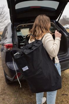 a woman carrying a large black bag into the back of a car