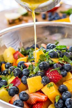 fruit salad being poured into a bowl with dressing