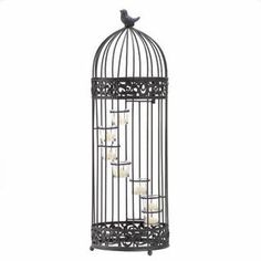 a black birdcage filled with candles on top of a white table next to a wall