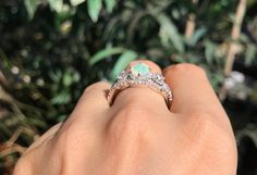 a woman's hand with a diamond ring on it and some bushes in the background