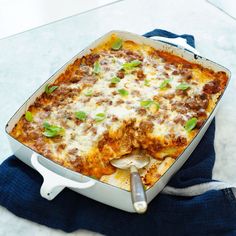 a casserole dish with meat, cheese and green onions in it on a blue towel