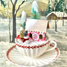 a teacup with a house in it on top of a saucer filled with snow