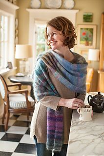 a woman standing in a kitchen with a coffee cup and blanket over her shoulders, wrapped in a shawl