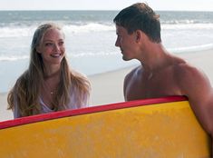 a man and woman standing on the beach with their surfboards looking at each other