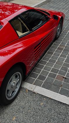 a red sports car parked on the side of the road next to a brick sidewalk