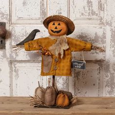 a scarecrow with a hat, coat and two pumpkins on a wooden table