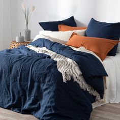 a bed with blue linens and orange pillows in a white walled room next to a wicker basket