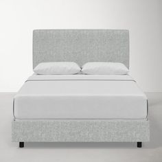 a bed with white sheets and pillows on top of it's headboard, in front of a gray wall