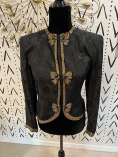 This vintage d'ore jacket is sure to turn heads. The jacket has a black jacquard floral print that has gold beaded bows down the center as well as gold trim along the collar, sleeves, and bottom hem. As seen in the pictures, the closure is hooks that attach to a threaded loop.  Size on tag: 6 Fits like a size 4 Please note, there are two areas on the jacket where beading is loose. This can be fixed quickly by hand sewing the beads tighter. Fitted Winter Outerwear With Gold Embroidery, Gold Outerwear With Long Sleeves And Gold Embroidery, Fitted Gold Embroidered Outerwear, Vintage Beaded Long Sleeve Outerwear, Luxury Beaded Vintage Outerwear, Gold Trim, Gold Beads, Hand Sewing, Tights