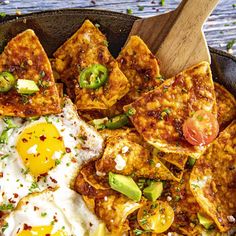 a skillet filled with eggs, tofu and other toppings next to a wooden spoon