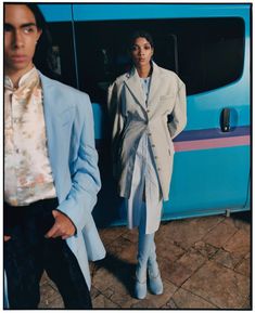 two people standing in front of a blue and white bus with one person wearing a suit