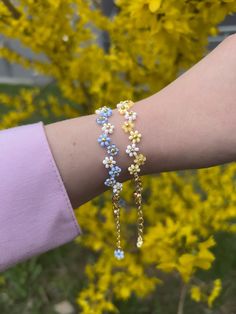 a woman's arm with two bracelets on it and yellow flowers in the background