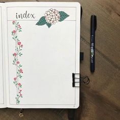 an open planner with flowers and leaves on it next to a black marker, pen and clipboard