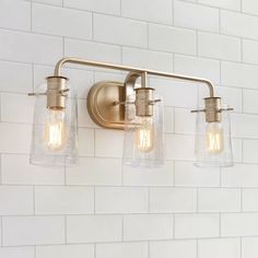 three light bathroom fixture with clear glass shades on the wall and white tile back splash