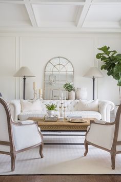 a living room filled with white furniture and a large mirror on the wall above it