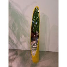 a large yellow mirror sitting on top of a floor next to a potted plant