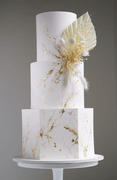 a three tiered white cake with gold leaf decoration