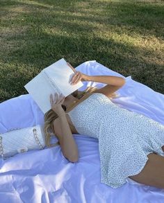 a woman laying on the grass reading a book