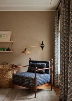 a blue chair sitting in front of a window next to a lamp and bookshelf