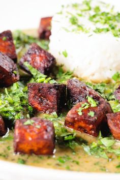 a white plate topped with tofu and rice covered in green garnishments