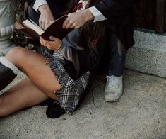 a woman sitting on the ground reading a book while wearing high heeled shoes and holding an open book