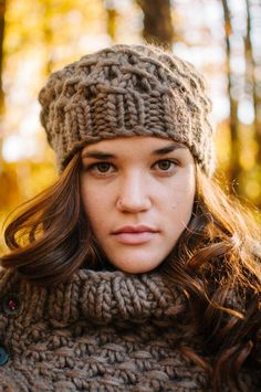 a woman with long hair wearing a knitted hat and scarf in an autumn forest