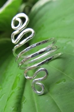 a silver spiral ring sitting on top of a green leaf next to a large plant