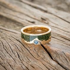 a gold ring with a blue stone in it on top of a piece of wood