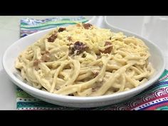 a white bowl filled with pasta and meat on top of a colorful table cloth next to a fork