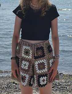 a woman standing on the beach with her hands in her pockets, wearing shorts and a black shirt