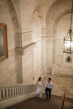 a man and woman are walking down the stairs in an old building with chandelier