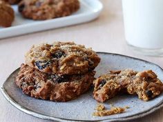 three cookies are on a plate next to a glass of milk and a tray of cookies