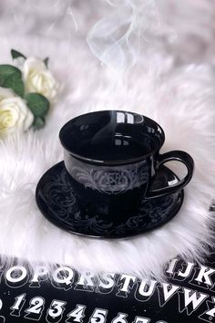 a black coffee cup and saucer sitting on top of a white fur covered table