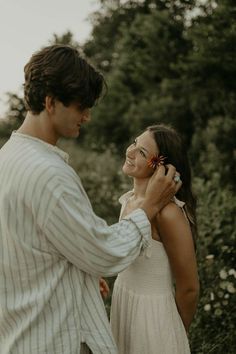 a man standing next to a woman talking on a cell phone while holding a flower in her hand