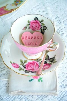 a pink heart shaped cookie sitting in a tea cup on top of a saucer