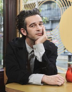 a man sitting at a table with his hand on his chin and looking off to the side